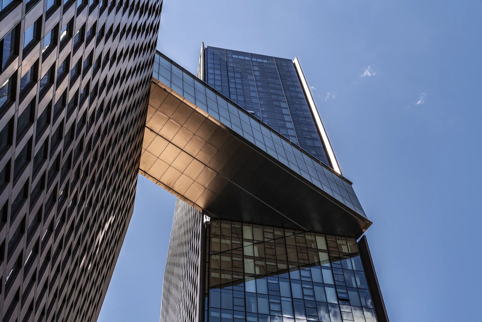 Seen from below, the two towers lean apart and the bridge crosses between them against open sky.